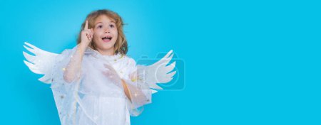 Téléchargez les photos : Child angel pointing up, point gesture. Valentine angel. Little cupid child. Kid angel with angels wings, isolated on blue studio background. Valentines day gift card. Banner header, copy space - en image libre de droit