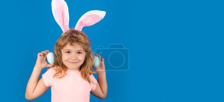Téléchargez les photos : Happy Easter. Kids boy in bunny ears hunting easter eggs isolated on blue background. Wide photo banner for website header design - en image libre de droit