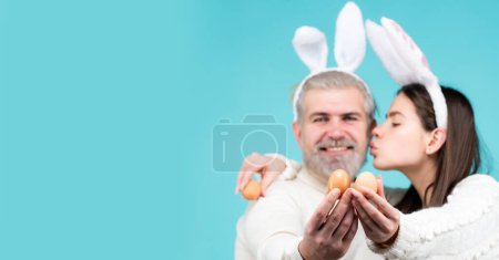 Foto de Couple with eggs for Easter. Happy couple with bunny ears and eggs on blue background isolated. Bunny couple with Bunny ears. Horizontal photo banner for website header design - Imagen libre de derechos
