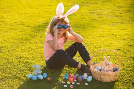 Junge mit Ostereiern und Hasenohren im Freien. Nettes Kind bedeckt Augen mit Eiern mit frohen Ostern im Park