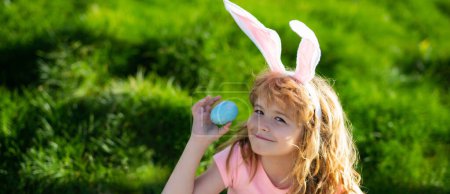 Téléchargez les photos : Easter bunny boy. Child in bunny ears hunting easter eggs outdoor on backyard. Easter egg hunt. Wide photo banner for website header design - en image libre de droit