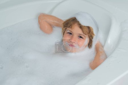 Foto de Children bathing. Kid bathing in a bath with foam. Funny kid face bathed in the bath - Imagen libre de derechos