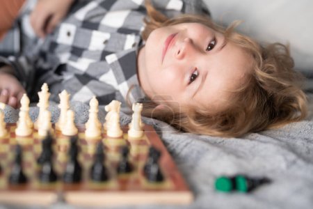 Téléchargez les photos : Cute child playing chess on bed at home. Portrait of clever kid with chessboard. Boy play chess - en image libre de droit