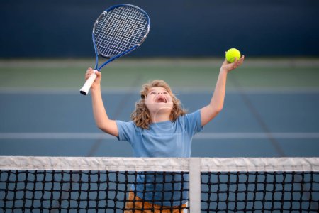 Foto de Child swinging racket while training on tennis. Child with racket and ball playing tennis on tennis court. Sport kids - Imagen libre de derechos