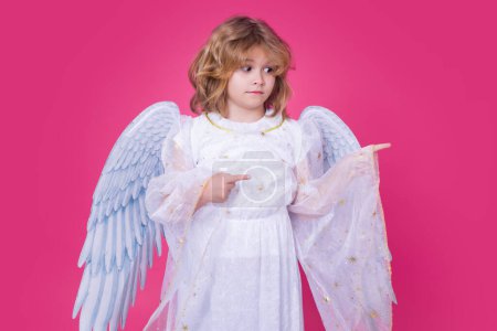 Foto de Child angel pointing finger, point gesture. Cute angel child, studio portrait. Angel kid with angels wings, isolated background - Imagen libre de derechos