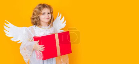 Foto de Cute blonde kid angel with gift box present. Beautiful little angel. Isolated studio shot. Cute Pretty child with angel wings. Banner header with copy space - Imagen libre de derechos