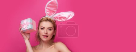 Photo for Portrait of a happy Easter girl holding present box isolated over pink background. Young woman with bunny ears. Easter banner, mockup copy space, header for website, template - Royalty Free Image