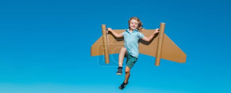 Photo for Happy child with paper wings against blue sky. Kid with toy jetpack having fun in spring green field outdoor. Freedom carefree and kids imagination dream concept - Royalty Free Image