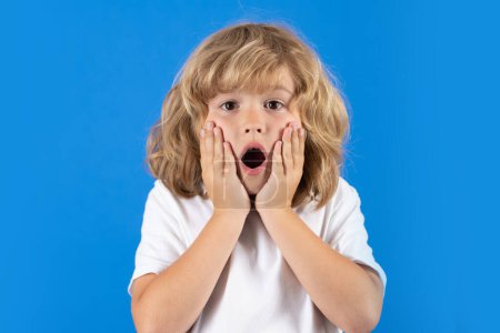 Téléchargez les photos : Shocked child keeping hands near cheek with open mouth on studio isolated background. Surprised face, excited emotions of child. Shock, omg and wow expression - en image libre de droit