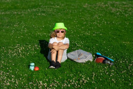 Foto de Kid on nature. Happy children rest fun outdoors. Kids relaxing in spring park. Boy sitting on green grass - Imagen libre de derechos