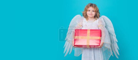 Foto de Cute child angel with gift box present. Child angel. Portrait of cute kid with angel wings isolated on studio background. Panoramic banner wide poster horizontal header - Imagen libre de derechos
