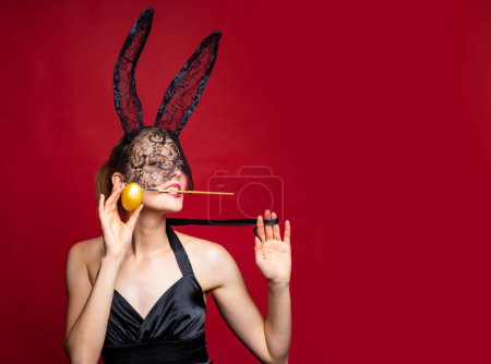Téléchargez les photos : Femme sexy lapin de Pâques portant un masque et des oreilles célébrant les vacances de Pâques. Jeune femme sensuelle provocatrice en costume de lapin isolé à fond rouge. Concept de lapin sexy - en image libre de droit
