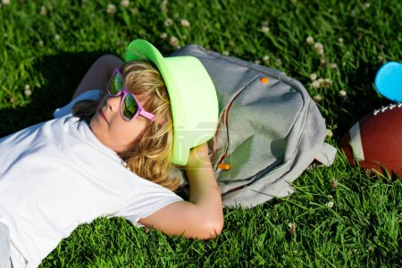 Foto de Summer holiday. Child relax at the summer park. Kid boy lying on green grass outdoor - Imagen libre de derechos