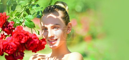 Foto de Portrait of sensual woman in spring background. Banner for website header. Happy girl in a garden with red roses. Beautiful young woman smelling a rose flower - Imagen libre de derechos