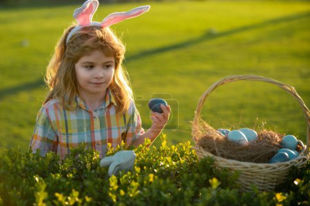 Photo for Child bunny boy with rabbit bunny ears. Child boy hunting easter eggs in backyard - Royalty Free Image