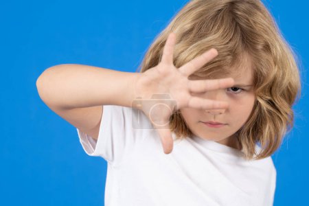 Téléchargez les photos : Close up portrait of child making stop gesture on isolated blue background. Kid showing warning symbol, hand sign no. Kids protection, bullying, abuse and violence concept - en image libre de droit