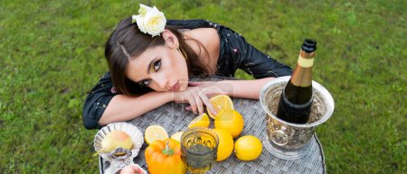 Foto de Sensual spring woman, banner for website header. Sexy woman on summer picnic on a grass in the park with wine and fresh fruits - Imagen libre de derechos
