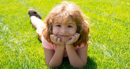 Téléchargez les photos : Close up portrait of a cute child laying in grass in summer nature park. Spring and kid. Wide photo banner for website header - en image libre de droit
