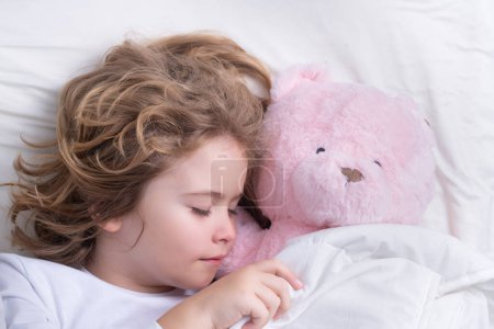 Foto de Cute child sleeping with a toy teddy bearon bed at home. Bedtime, kid sleeps. Kid asleep on soft pillow with blanket having healthy sleep - Imagen libre de derechos