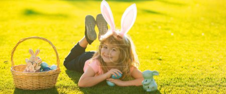 Foto de Happy easter bunny child boy. Horizontal photo banner for website header design. Kids in bunny ears on Easter egg hunt in garden - Imagen libre de derechos