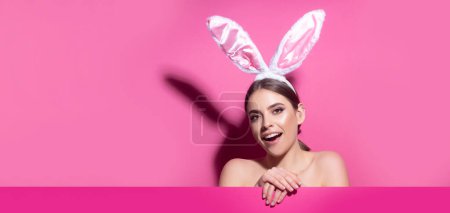 Foto de Easter bunny woman with rabbit ears. Beautiful young girl with on pink blank poster. Wide photo banner for website header design - Imagen libre de derechos