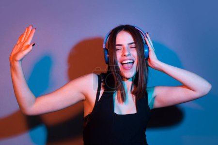 Photo for Dj girl. Portrait of excited attractive girl in headphones listening music isolated on studio background. Studio portrait of girl in headphones on neon light. Favorite music and song - Royalty Free Image
