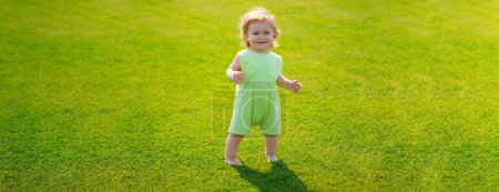 Photo for Baby on spring grass field, banner. Little baby learning to crawl steps on the grass. Concept childrens months. Happy child playing on green grass playground. First step - Royalty Free Image