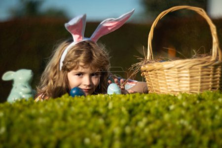 Téléchargez les photos : Lapin de Pâques enfant chasse oeufs en plein air Bonne journée de Pâques, Garçon enfant posé sur l'herbe dans le parc - en image libre de droit