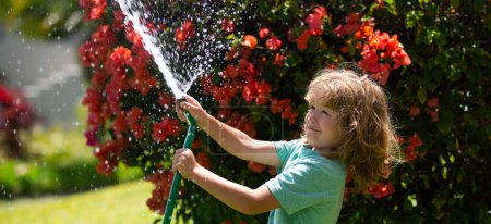 Téléchargez les photos : Spring child watering, banner. Cute little boy watering flowers in the garden at summer day. Child farmer with garden hose in planting plant. hose. Funny kid watering plants in the yard garden - en image libre de droit