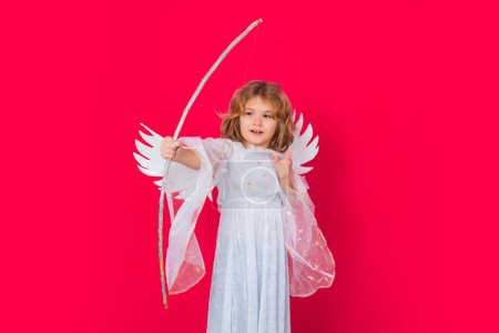 Photo for Angel kid shoots a love arrow from a bow on Valentines Day. Child at angel costume. Kid with angel wings. Isolated studio shot - Royalty Free Image