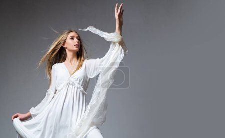 Téléchargez les photos : Movement model in white dress. Fashion photo of a beautiful young woman in a pretty dress over studio background. Fashion model, elegant woman in fashion dress posing in the studio - en image libre de droit