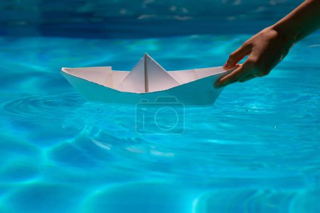 Foto de Paper boat with hand. Paper boat sailing on blue water surface. Concept of tourism, travel dreams vacation holiday, dreaming traveling, sailing adventure - Imagen libre de derechos