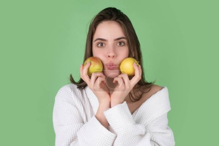 Téléchargez les photos : Young girl with kissing lips holding apple on blue studio background. Healthy lifestyle and nutrition, dieting, weight loss, cosmetology, dental care and healthy teeth. Close up woman portrait - en image libre de droit