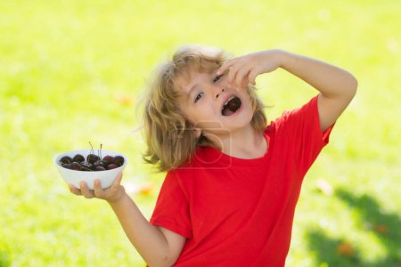 Photo for Child boy hold plate cherries in park. Cherry for kids. Summer background with green grass - Royalty Free Image