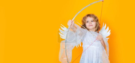Photo for Angel child shoots a love arrow from a bow on Valentines Day. Kid wearing angel costume white dress and feather wings. Innocent child. Wide banner panoramic header - Royalty Free Image