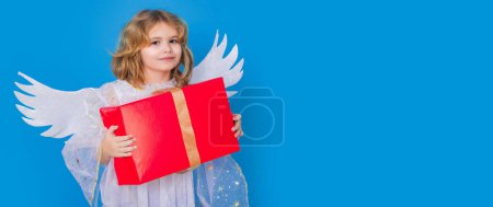 Photo for Kid boy angel with gift box present. Valentines day. Blonde cute child with angel wings on a blue isolated studio background. Banner header with copy space - Royalty Free Image