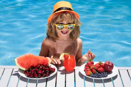 Foto de Summer fruit. Child eating fruits near swimming pool during summer holidays. Kids eat fruit. Healthy fruits for children. Summer vacation with children. Strawberry, watermelon, cherry and blueberry - Imagen libre de derechos