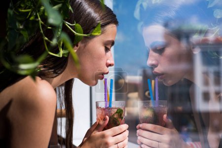 Téléchargez les photos : Sensual young woman drinking red lip cocktail, looking out window - en image libre de droit