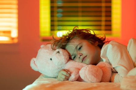 Téléchargez les photos : Cute drowsy sleepy child with toy teddy bear in bed, bedtime, childhood and growth kids concept, close-up indoor portrait. A sleepy child - en image libre de droit