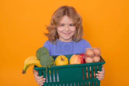 Téléchargez les photos : Portrait of child with shopping basket purchasing food in a grocery store on studio isolated background. Sale and discount - en image libre de droit