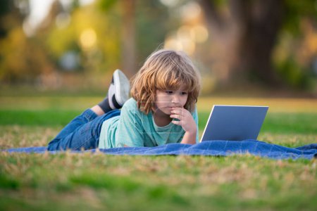 Foto de School boy in park outdoor doing school homework. Child using laptop. Self education learning studying. Early development for children - Imagen libre de derechos