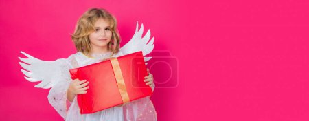 Photo for Kid boy angel with gift box present. Little cute child at angel costume on isolated background. Banner for website header design - Royalty Free Image