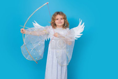 Photo for Angel kid shoots a love arrow from a bow on Valentines Day. Portrait of cute kid with angel wings isolated on studio background. Little angel, valentines day. Angelic kids - Royalty Free Image