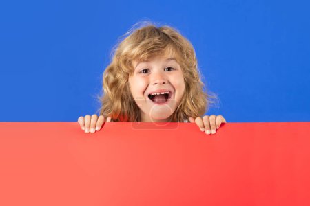 Photo for Excited kid boy on studio isolated background. Child hold red blank banner on studio background. Advertising billboard, placard, copy spase. Poster for your text - Royalty Free Image