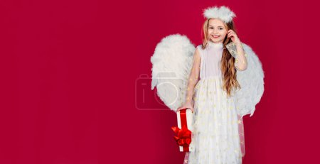 Téléchargez les photos : Valentines day banner with angel child. Kid girl angel with present gift, studio portrait. Little angel with white wings holds gift. Playful angelic little girl. Valentines day - en image libre de droit