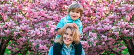 Photo for Mother and son near blossom sakura tree background. Spring family banner. Cute child hugging his mother. Cute boy sitting on mothers shoulders - Royalty Free Image