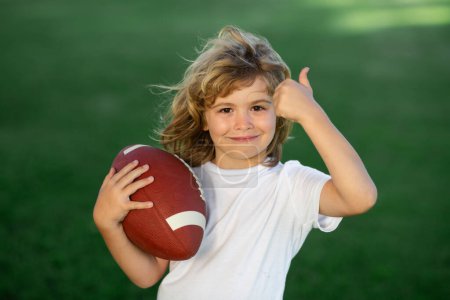 Téléchargez les photos : Outdoor kids sport activities. Child boy with american football, rugby ball. Cute portrait of a american football player, outdoor - en image libre de droit