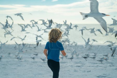 Photo for Happy childhood. Child chasing birds near summer beach. Excited boy running on the beach with flying seagulls birds - Royalty Free Image