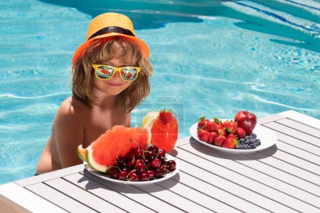Foto de Kid on summer vacation. Kid having fun in swimming pool. Summer vacation and healthy lifestyle concept. Child with fresh cocktail and fruits - Imagen libre de derechos