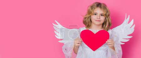 Téléchargez les photos : Angel kid with heart. Valentines day. Blonde cute child with angel wings on a pink studio background. Banner header, copy space - en image libre de droit